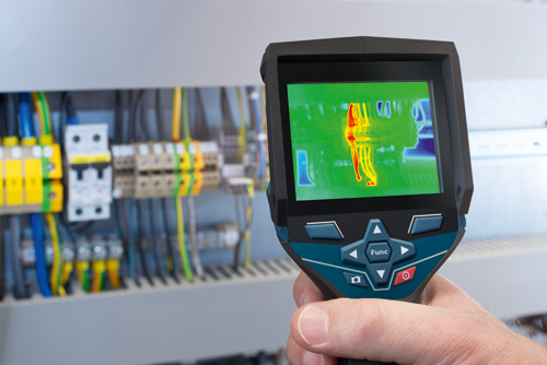 Hand holding a thermal imaging camera pointed at an electrical panel, with "Func" button and power button visible. The thermal image shows heat patterns.