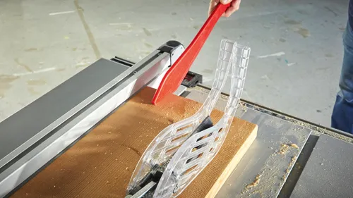 Person using a table saw, with a red push stick and a clear blade guard cutting a piece of wood.