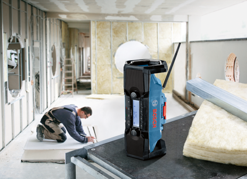 A person kneels near a construction project, with a Bosch radio and insulation visible.