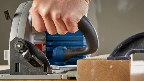 Bosch circular saw cutting wood, held by a person's hand.