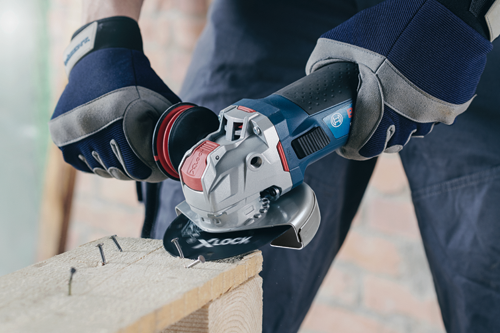 Bosch X-LOCK power tool cutting into a wooden plank with nails; gloved hands