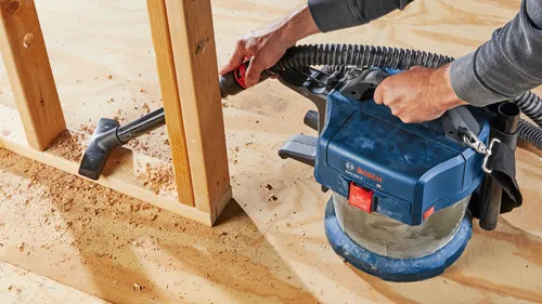 Person using a Bosch GAS18V-3 vacuum to clean sawdust from a wooden frame.