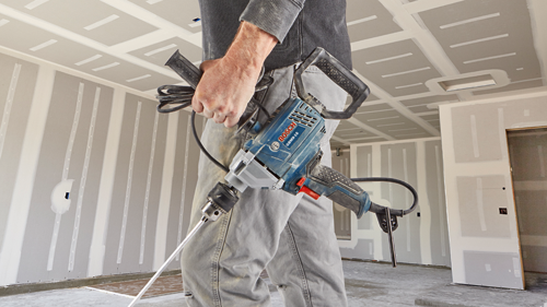 Bosch GBM9-16 drill held by a person in a construction setting.