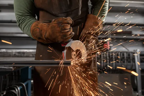 Person wearing protective gear using a grinder, sparks flying.