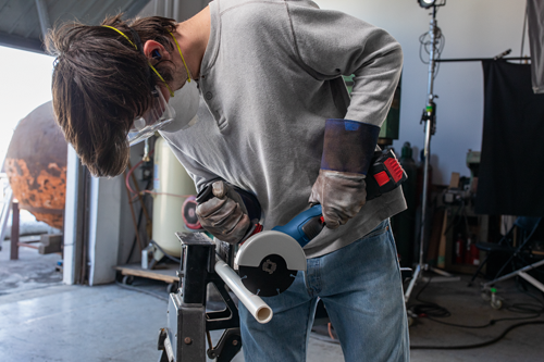 Person wearing protective gear using a Bosch angle grinder to cut a pipe.