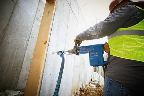 Bosch 11316EVS rotary hammer being used to drill into a concrete wall. Person wearing work gear.