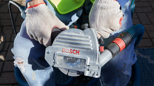 Bosch electric saw, with "BOSCH" logo, with a circular blade, held by a person wearing work gloves.