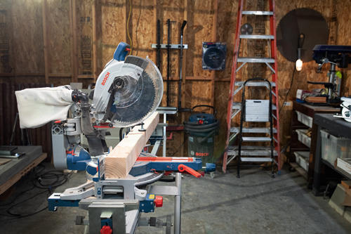 Bosch miter saw with a General Purpose blade cutting a piece of lumber in a workshop.