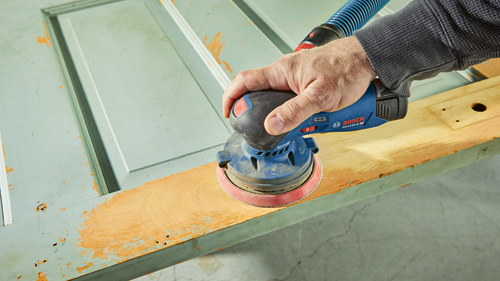 Bosch GEX12V-5 HD orbital sander being used on a weathered wooden surface.
