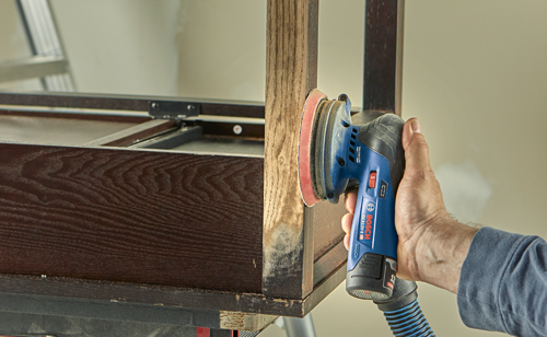 Bosch GEX12V-5, 203C.A. cordless sander being used to sand a wooden surface.
