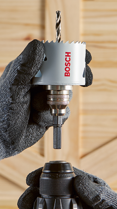 Bosch hole saw with 'BOSCH' text held by gloved hands, above a drill chuck.