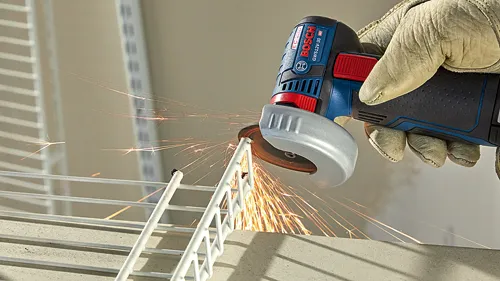 Bosch GWS12V-30 HD angle grinder in use, cutting metal. Sparks are flying from the tool. The tool is being held by a gloved hand.