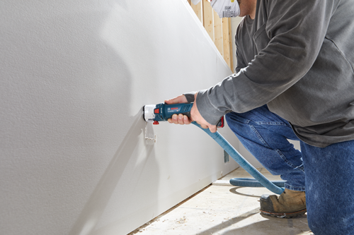 Bosch GCU18V-30, person cutting into drywall with a saw and vacuum hose, wearing a mask.