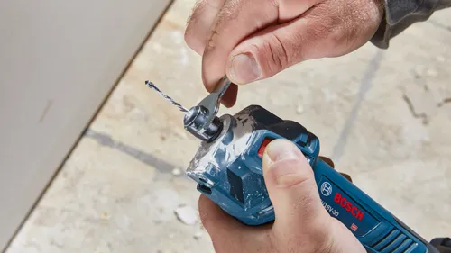 Person holding a Bosch U18V-30 tool, using a wrench on the drill bit.