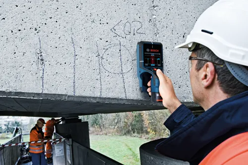Bosch concrete scanner in use by a person wearing a white helmet; two other people are working in the background.