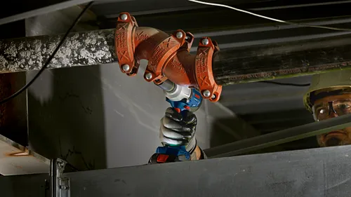 Bosch cordless impact wrench being used to tighten a pipe joint, with text "VICTAULIC FireLock" and "ALLIED DYNA FLOW ABF 3 300PSIUSA"