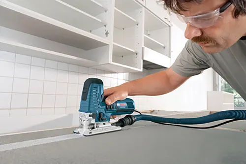 A person using a jigsaw to cut a countertop, wearing safety glasses.