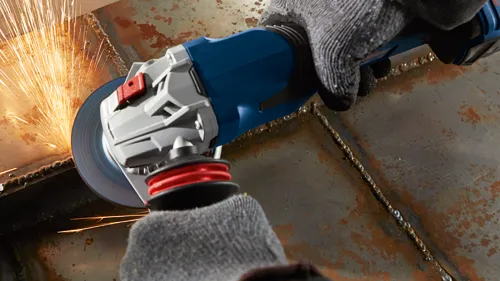Person wearing gloves using a grinder tool, sparks flying as it grinds the metal.
