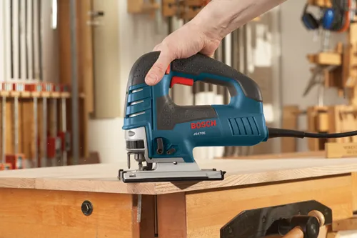 Bosch JS470E jigsaw being held over a wooden work surface.