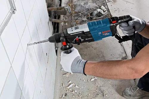 Bosch Bulldog Xtreme Max rotary hammer drilling into tile, a person wearing work gloves using the tool.