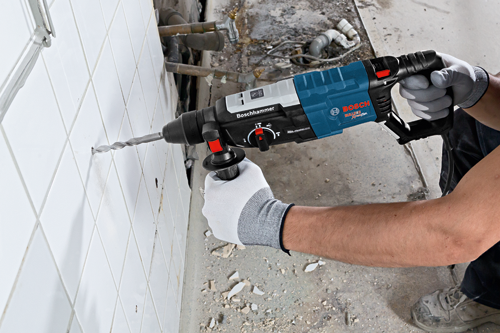 Bosch Bulldog Xtreme Max rotary hammer drilling into tile, a person wearing work gloves using the tool.