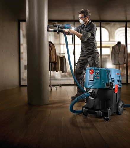 A person drills a column with a Bosch drill and a vacuum cleaner. Visible text on the vacuum cleaner: "BOSCH", "VAC35L", "AFC", "Automatic Filter Cleaning".