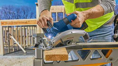 Bosch circular saw cutting wood; person wearing safety vest and jeans.