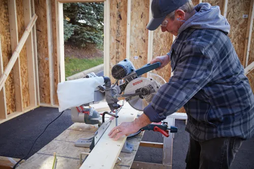 Person wearing safety glasses and hearing protection, using a Bosch miter saw to cut wood.