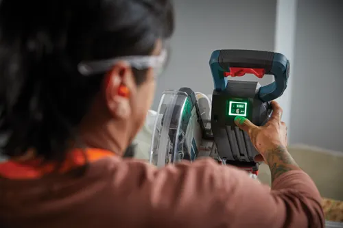Person wearing safety glasses and ear protection operating a miter saw; the saw display shows "ECO".