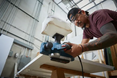 Bosch PL1632 power planer being used by a person, wearing safety glasses and earplugs.