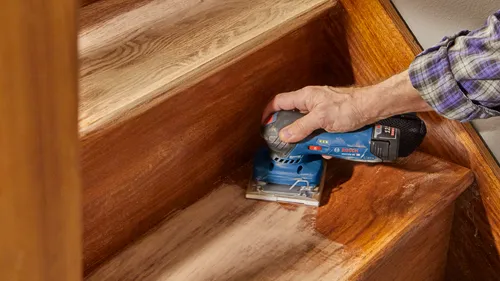 Person sanding wooden stairs with a Bosch GSS12V-40 HD sander.