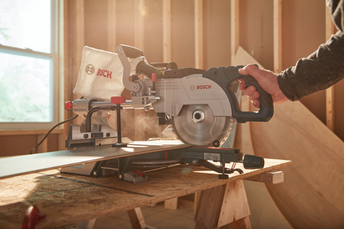 Bosch miter saw with a blade cutting a piece of wood, a person's hand holding the saw handle.