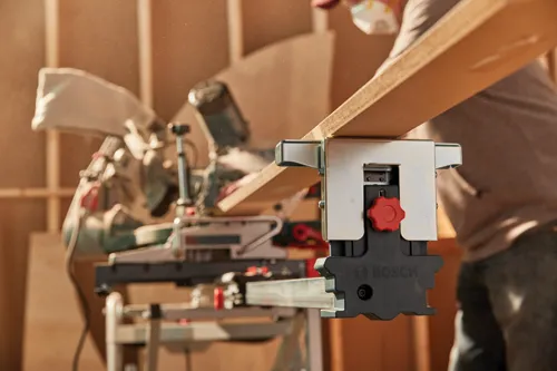 Bosch miter saw cutting wood, person wearing mask in background.