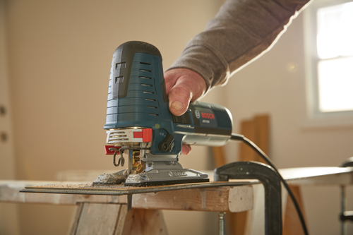 Bosch jigsaw, being used to cut a piece of wood. The person is wearing a gray long-sleeve shirt.