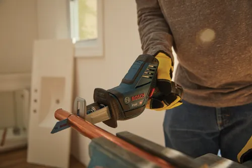 Man using the Bosch cordless PS60 reciprocating saw to cut copper pipe being held by a vice.