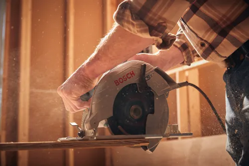 Bosch circular saw cutting wood, person wearing a plaid shirt and jeans.