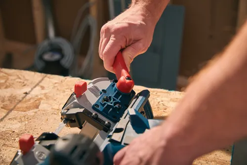 A person uses a circular saw with a red handle to cut wood.