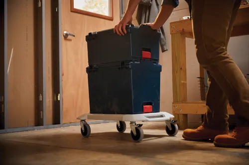 A person moves two stacked dark blue toolboxes with red latches on a rolling cart.