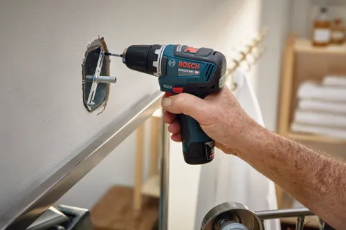 Bosch GSR12V-300 HD cordless drill being used to install a metal bracket in a wall.