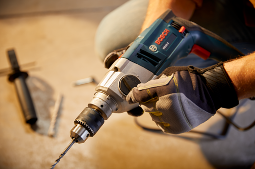 Bosch HD18-2 drill held by a person wearing gloves. The drill bit extends forward.