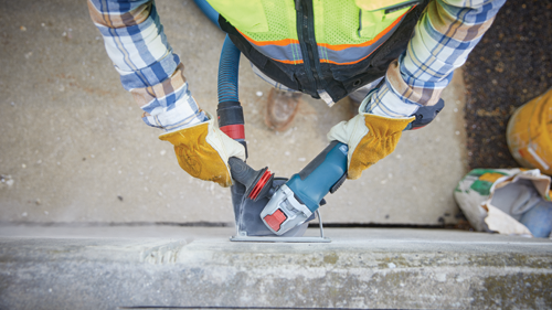 Person wearing gloves and safety vest using a grinder on concrete.
