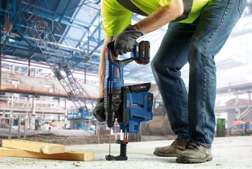 Bosch BULLDOG GBH18V-26D cordless rotary hammer drill with CORE18V.4Ah battery, being used by a person wearing work gloves and jeans at a construction site.