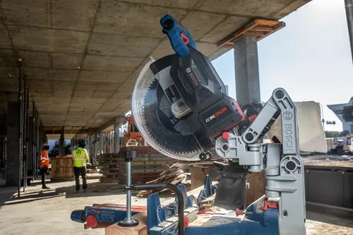 Bosch miter saw with 18V 12Ah battery, and two construction workers standing in the background.