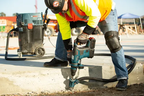 Bosch GBH18V-36C BITURBO rotary hammer drilling a concrete surface, connected to a Bosch HDC300 dust extractor, a person wearing safety gear at a construction site.