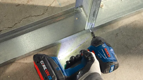Bosch GDR18V-1860C brushless impact driver being used to fasten a screw into a metal stud, with a CORE18V 4Ah battery attached.