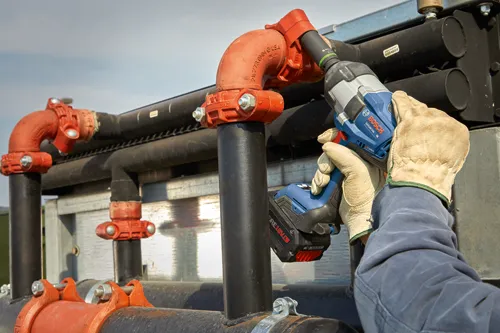 Bosch GDS18V-740 cordless impact wrench being used on orange piping; a person wearing gloves holds the tool.