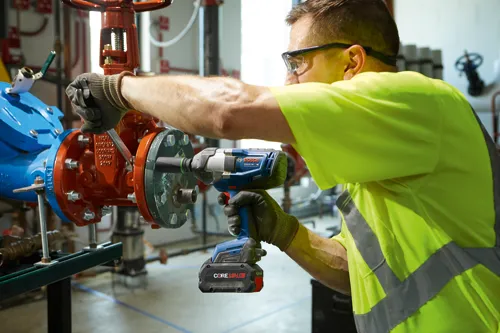 A person wearing safety glasses and a neon yellow vest using a Bosch GDS18V-740 Turbo Brushless impact wrench, with CORE18V 8.0Ah battery on a pipe assembly.
