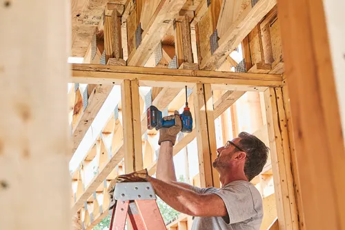 Man with a Bosch cordless impact driver drilling in wood frame.