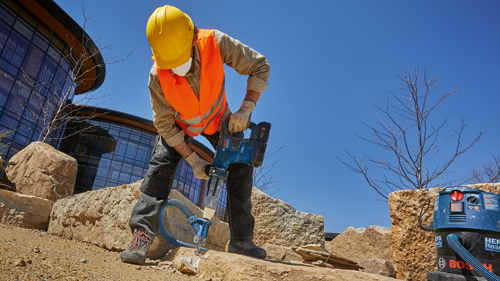 Person wearing a safety helmet and vest, using a Bosch tool to work on stone, with a HEPA Ready vacuum cleaner visible.