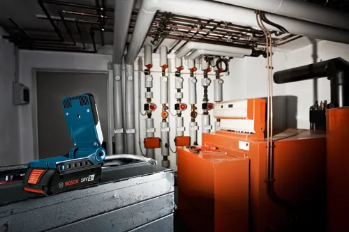 Bosch 18V 2Ah work light, on a metal surface, with pipes and equipment in background.
